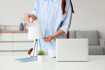 Young woman screwing light bulb into table lamp at home
