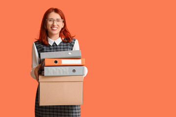 Young happy redhead businesswoman holding cardboard box with belongings and folders against orange...