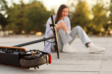 Young woman fallen off electric kick scooter in park