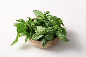 Wooden bowl with fresh green basil leaves on white background