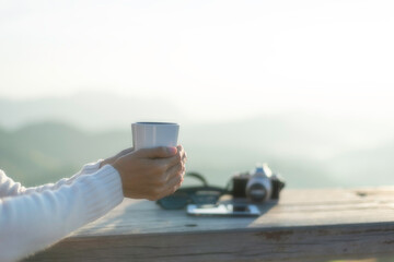 Woman drinking coffee while looking at a beautiful foggy mountain and nature view and camping at forest mountain on holiday vacation.