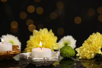 Diya lamps with candles and chrysanthemum flowers in water on black background against blurred...