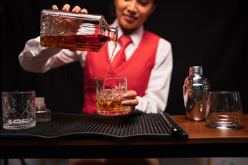 Bartender woman pours whiskey into a glass in a restaurant.	
