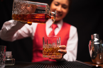  Bartender woman pours whiskey into a glass in a restaurant.