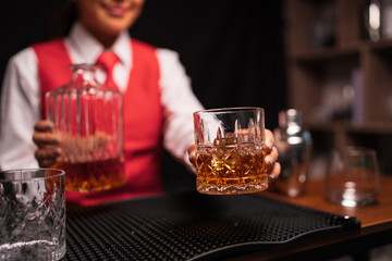 Bartender woman pours whiskey into a glass in a restaurant.	
