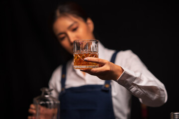  Bartender woman pours whiskey into a glass in a restaurant.