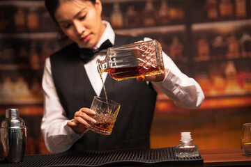 Bartender woman pours whiskey into a glass in a restaurant.	
