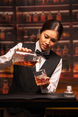  Bartender woman pours whiskey into a glass in a restaurant.