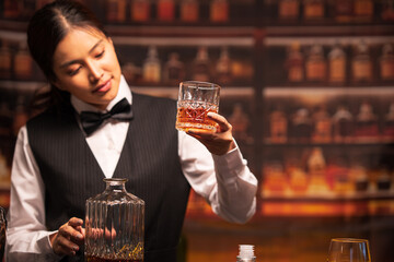 Bartender woman pours whiskey into a glass in a restaurant.	
