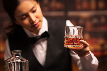  Bartender woman pours whiskey into a glass in a restaurant.
