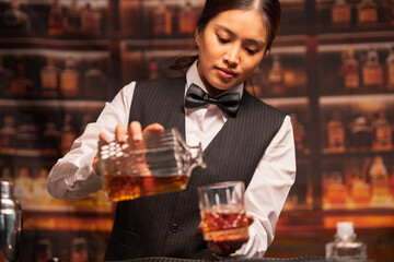  Bartender woman pours whiskey into a glass in a restaurant.