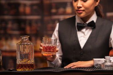 Bartender woman pours whiskey into a glass in a restaurant.	
