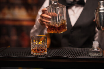 Bartender woman pours whiskey into a glass in a restaurant.	
