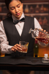 Bartender woman pours whiskey into a glass in a restaurant.	