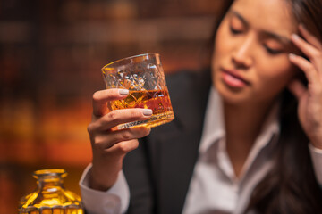 Asian woman in a black suit sitting holding a glass of whiskey at night in a restaurant.