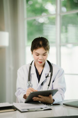 A female doctor works at her desk in a modern hospital office, using a laptop for patient records, consultation, and healthcare support.