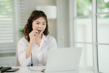 Obraz premium A young woman wearing a headset works at a desk in a call center, smiling as she provides customer support and online assistance.