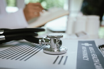 A doctor sits at a desk in a hospital office with stethoscope, documents, and laptop, providing healthcare consultation and care.