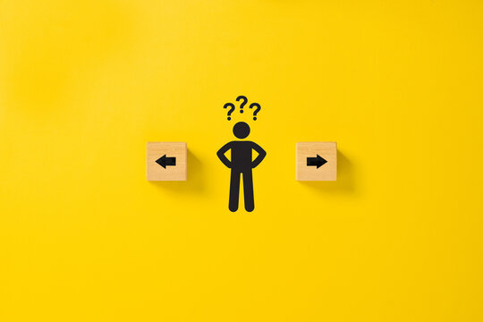 Decision making and choosing the right path. Confusion about deciding which direction to go. Stickman with question marks standing in between the wooden cubes with arrow symbols - Powered by Adobe