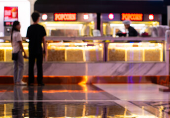 Blurred cinema concession stand with customers buying popcorn and drinks under colorful neon lighting at movie theater