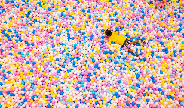 Child playing in colorful ball pit with thousands of multicolored plastic balls at indoor playground entertainment center