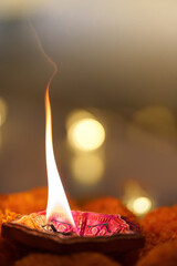 Diwali Festival. A glowing diya lamp with a dancing flame amidst marigold flowers.