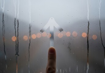 Finger drawing an arrow on a foggy window with city lights behind