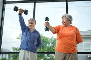 Happy mature couple exercising at home gym, Senior Asian couple working out with dumbbells in a home, Elderly man and woman doing bicep curls together for a healthy lifestyle