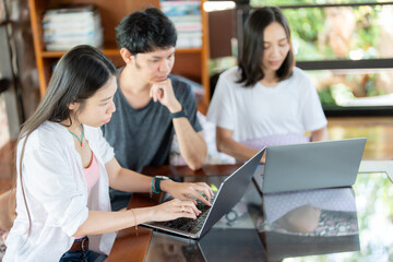 Obraz premium Inside the classroom, 3 Asian students plan a project using a laptop, discussing how education can be applied to industry and how those skills will impact their future careers.