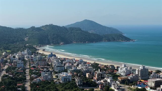 Aerial panorama revealing Mariscal beach, coastal cityscape merging with turquoise Atlantic waters, verdant mountains framing scenic landscape in Santa Catarina, Brazil