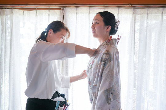 A woman is getting her clothes altered by another woman. The woman being altered is wearing a kimono