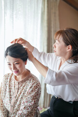 Fototapeta premium A woman is sitting on a chair while another woman is combing her hair. The woman getting her hair done is smiling, indicating that she is happy with the service