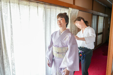 Obraz premium A woman in a kimono is getting her hair done by another woman. The scene is set in a room with a window and a curtain. Scene is calm and peaceful, as the two women are focused on their task