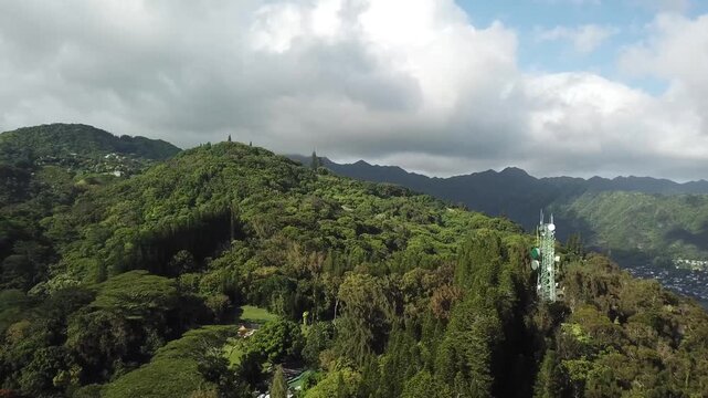 Transmission tower at dense growing Maliki valley trail surrounds by green mountains near Honolulu, Hawaii. Aerial wide shot.