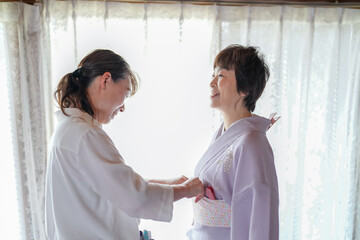 Obraz premium A woman in a kimono is being helped by a woman in a white shirt. The woman in the white shirt is helping the woman in the kimono adjust her clothing. Scene is one of care and assistance