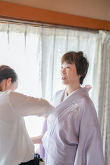 Obraz premium A woman in a purple kimono is being helped by a man. The woman is wearing a white shirt underneath her kimono