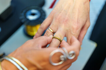 Close up of hands placing a gold ring on a finger, showcasing the process of ring selection and fitting in a jewelry workshop