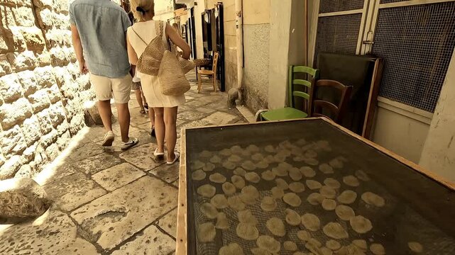 Narrow streets of Bari, Italy, where traditional handmade pasta is prepared, filmed with a quick pass over the tables of finished products and tourists in the background. Bari, Puglia, Italy, 21 juli 