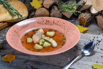 Salmon soup in a pinkish plate on a wooden background with a spoon