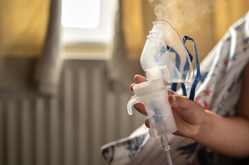 Close-up of a child hand holding a nebulizer inhaler mask while steam rising from the device....