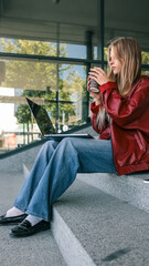 Young woman with a coffee cup using a laptop outdoors on a sunny day.