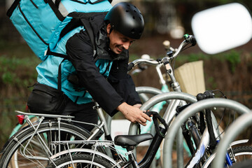 Deliveryman securing his bicycle with chain lock after delivery round