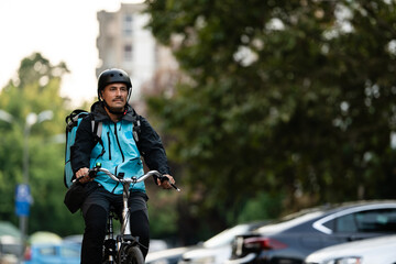 Naklejka premium Delivery man riding bicycle in city, delivering food, wearing helmet