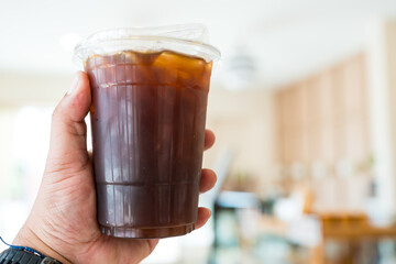 Hand holding ice black coffee in plastic glass at coffee shop.