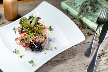 fresh salad with meat and prunes in a white plate macro photo