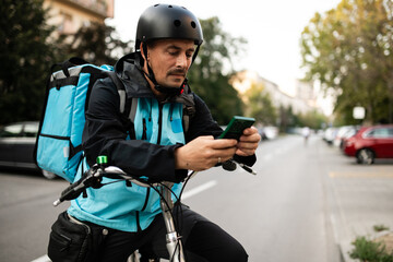 Deliveryman using smartphone and riding bicycle on city street