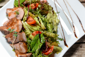 fresh salad with tomatoes and meat in teriyaki sauce in a white plate macro photo