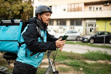 Delivery man using smartphone and carrying backpack on bicycle