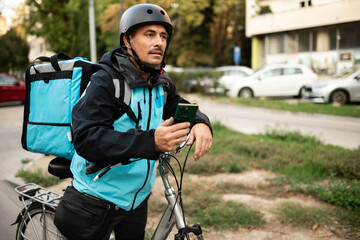 Deliveryman checking his smartphone and leaning on his bicycle