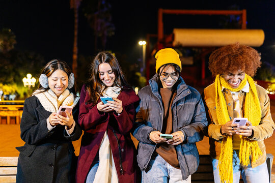 Happy millennial people having fun using smart phones devices together outdoors on winter. Social media and communication concept